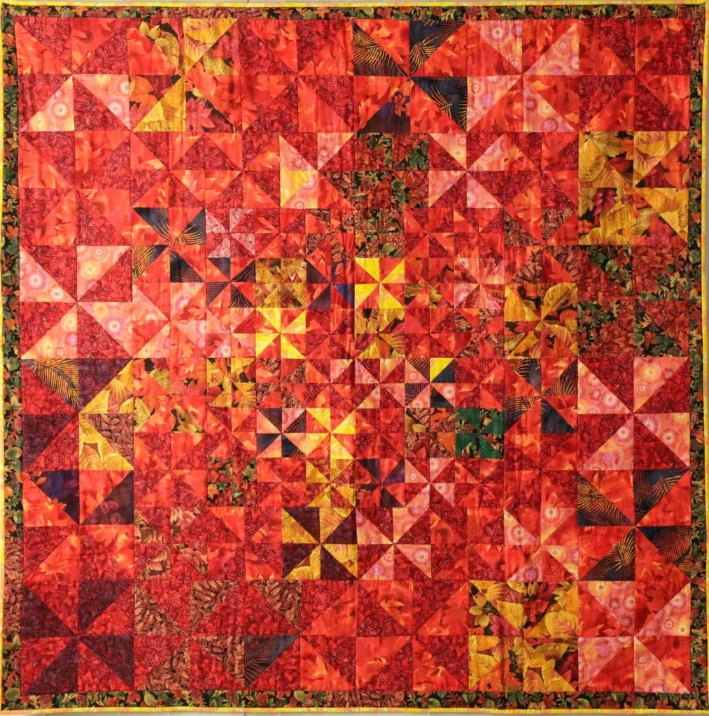 Quilt with triangles of fabric, primarily in shades of red with some yellow mixed in, arranged in pinwheel patterns