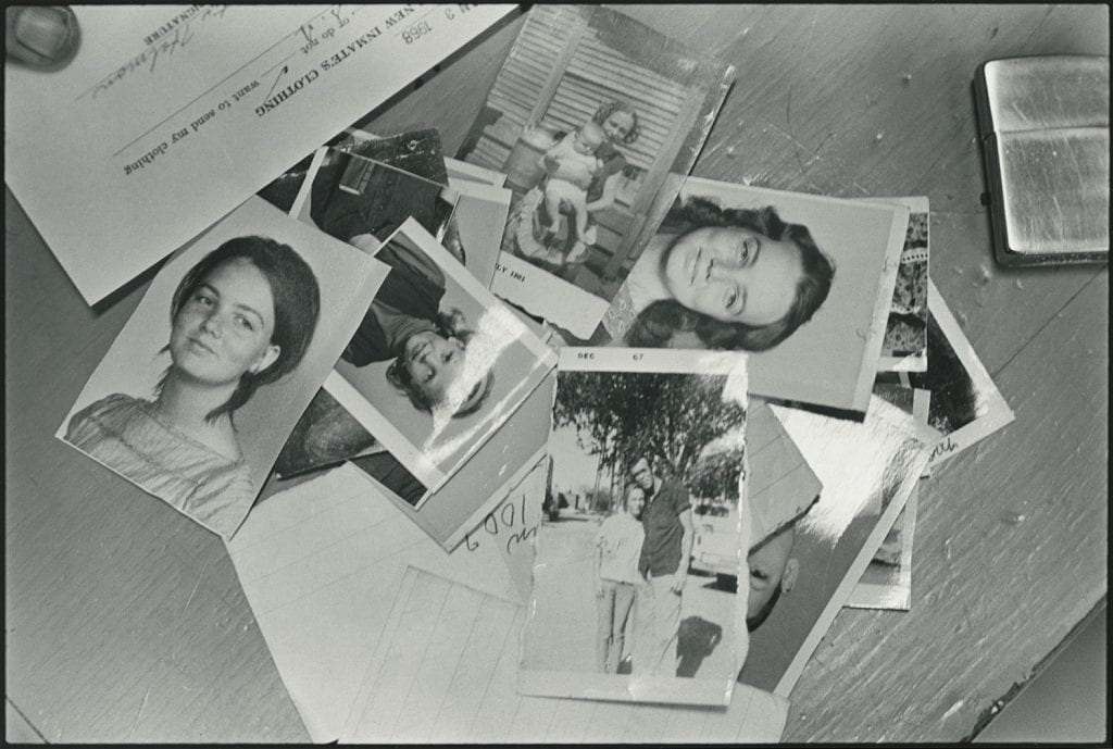 Black-and-white photograph of snapshots, including portraits of young white women, in a pile, with a lighter, scraps of paper, and a form labeled New Inmates Clothing